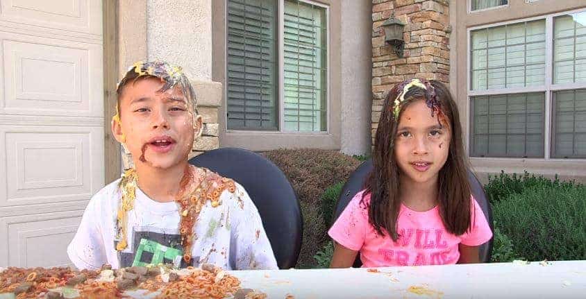 Two children playfully decide whether to eat or wear the food smeared on their faces.