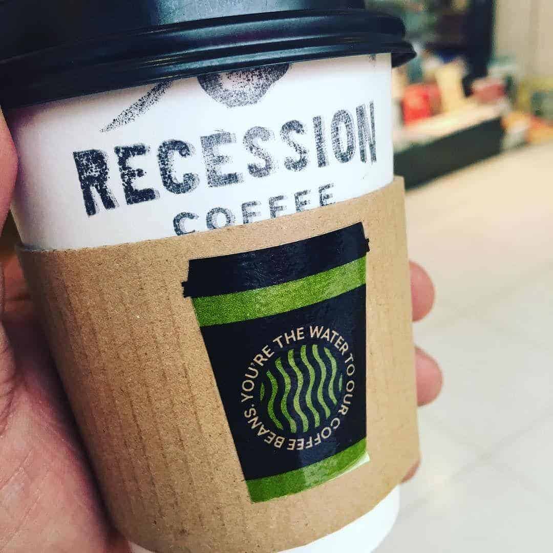 A person holding a cup of coffee that says #recessioncoffee, questioning its value in the midst of an economic downturn.