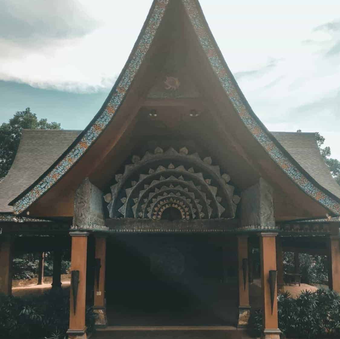 A traditional Southeast Asian pavilion with a high, ornate, tiered roof set against a background of trees.