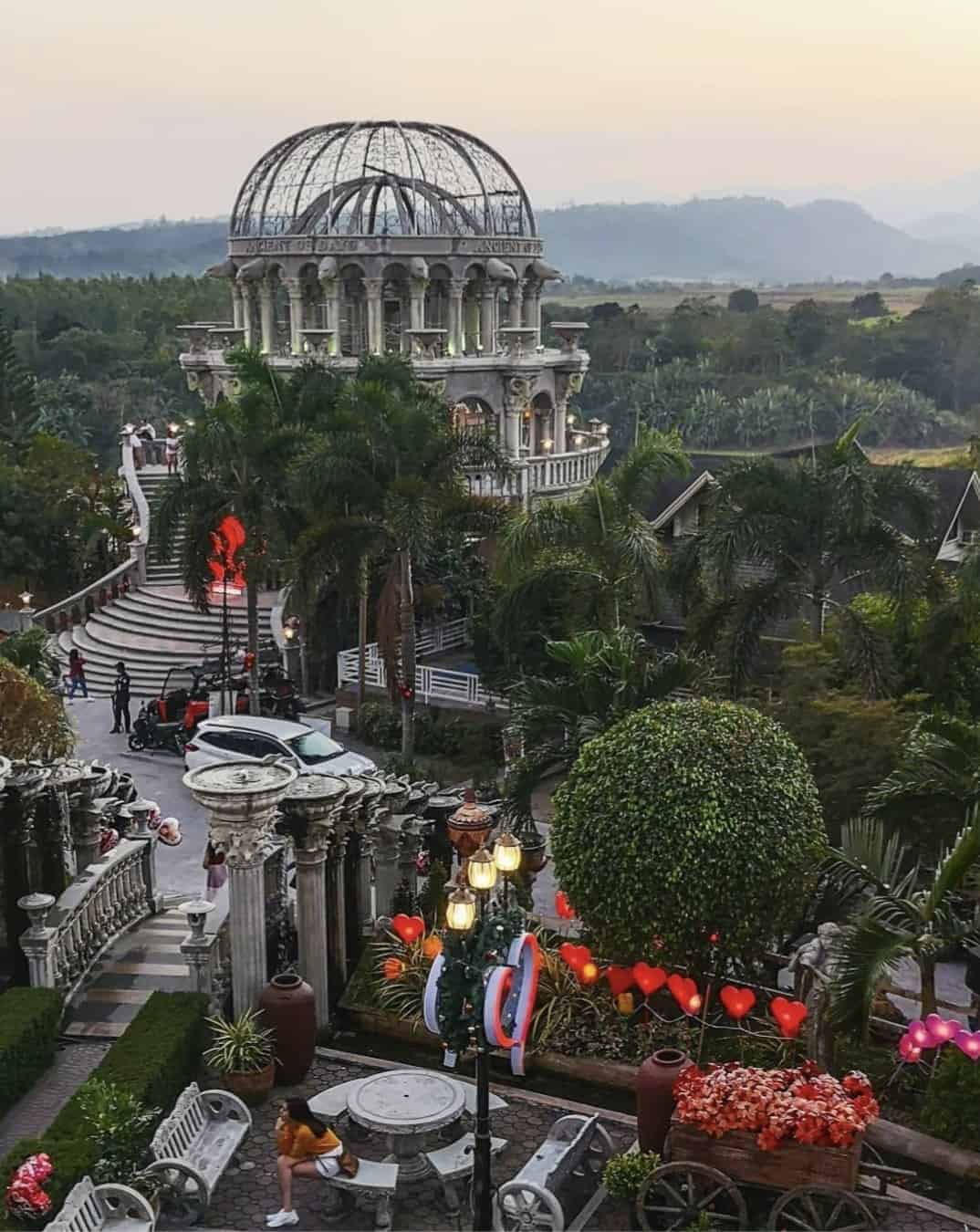 A romantic garden scene with a domed gazebo, palm trees, and heart decorations at sunset.