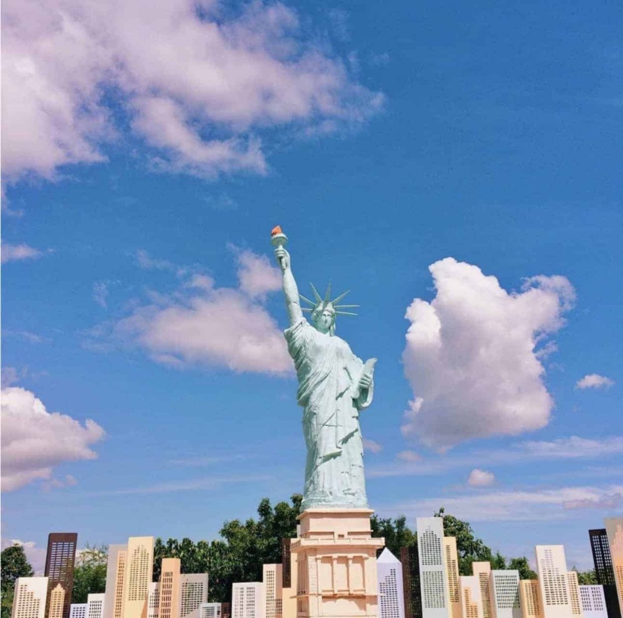 A small-scale model of the Statue of Liberty under a bright blue sky with scattered clouds.