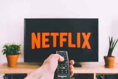 A hand holding a remote control points at a TV screen displaying the Netflix logo.