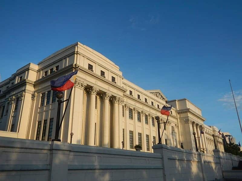 A grand neoclassical building with columns, Russian flags, and a clear blue sky.
