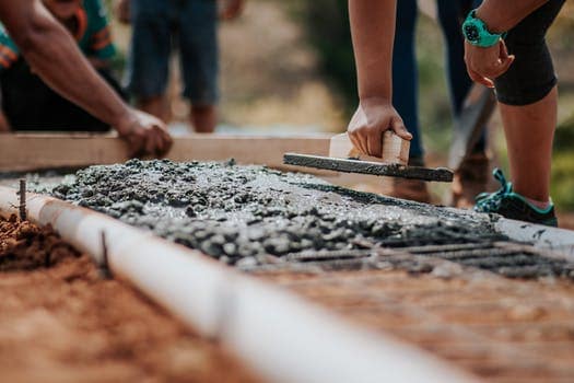 People smoothing wet concrete on a construction site with tools, focus on hands and rough surface.