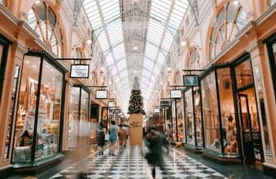 Elegant indoor shopping mall with glass ceiling, decorated with a large Christmas tree and people walking.