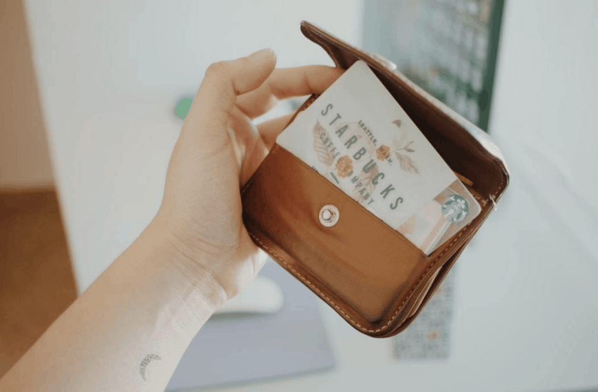 A woman's hand holding a new brown leather wallet with a Starbucks reward card.