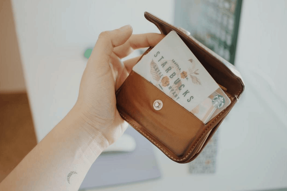 A woman's hand holding a new brown leather wallet with a Starbucks reward card.