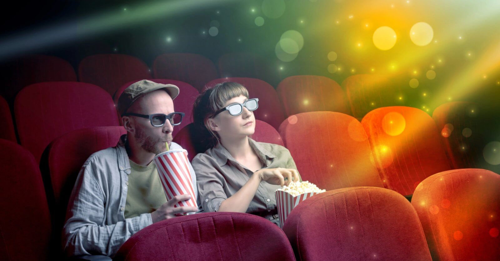 A man and woman wearing 3D glasses watch a Pinoy movie in a theater filled with colorful lights savoring popcorn and a drink