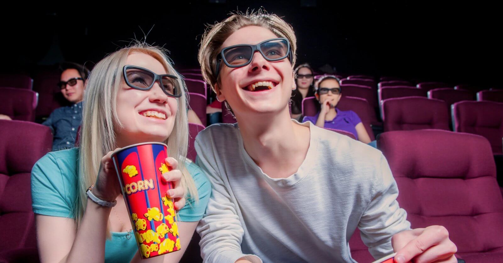 Teens wearing 3D glasses and smiling while watching a Pinoy movie in a theater with popcorn in hand surrounded by others