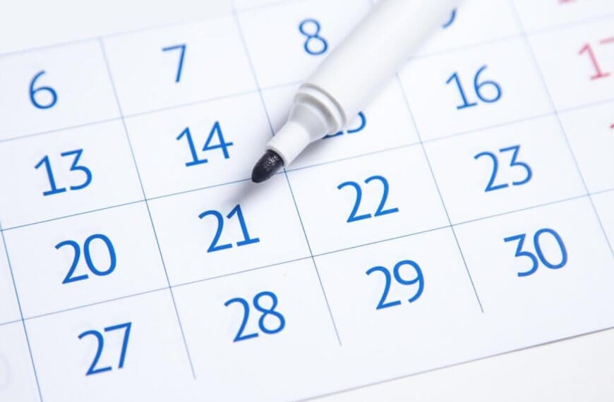 A close-up image of a 2025 Social Media Holiday Calendar showing the days of a month. The dates are in blue, except for weekends, which are in red. A white marker with its cap removed rests on "21," indicating it might be of importance. The days are printed in a grid layout, reminiscent of typical calendars used in the Philippines.