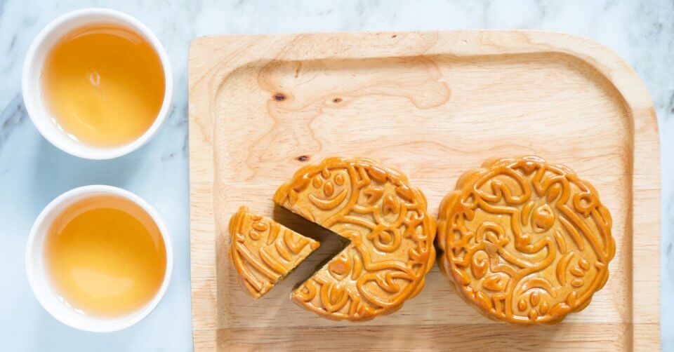 two mooncakes on a cutting board with two cups of tea at the mid autumn festival.
