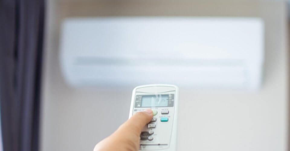 guide to choosing the right ac for your home with a person holding a remote control in front of an air conditioner.