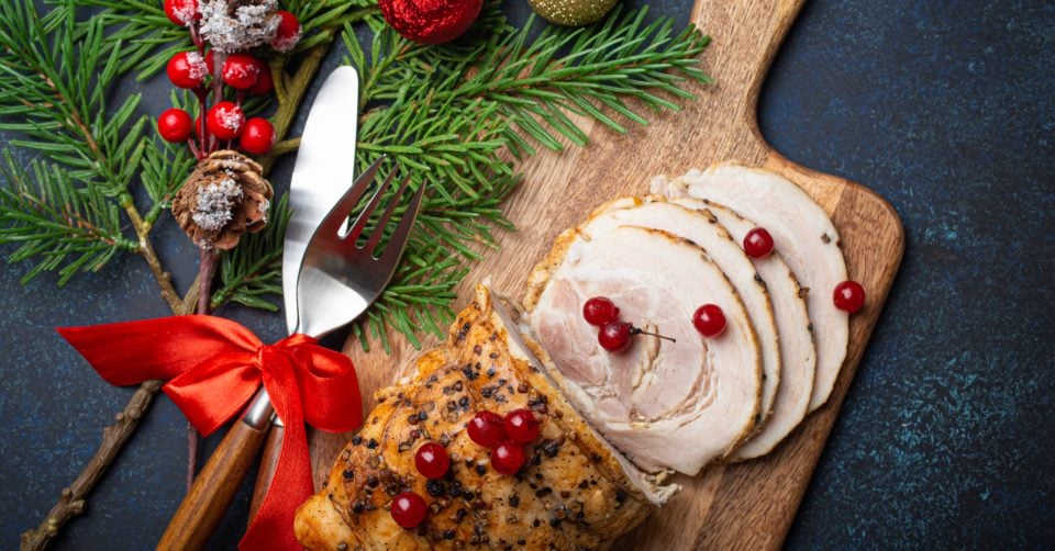 a festive christmas turkey on a cutting board with cranberries and a fork.
