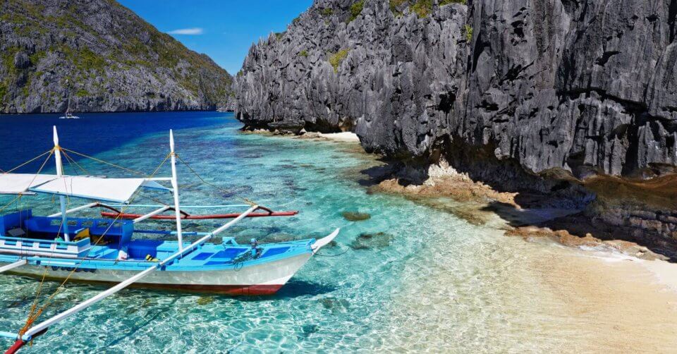 a summer destination in the philippines, a boat docked on a beach near a cliff.