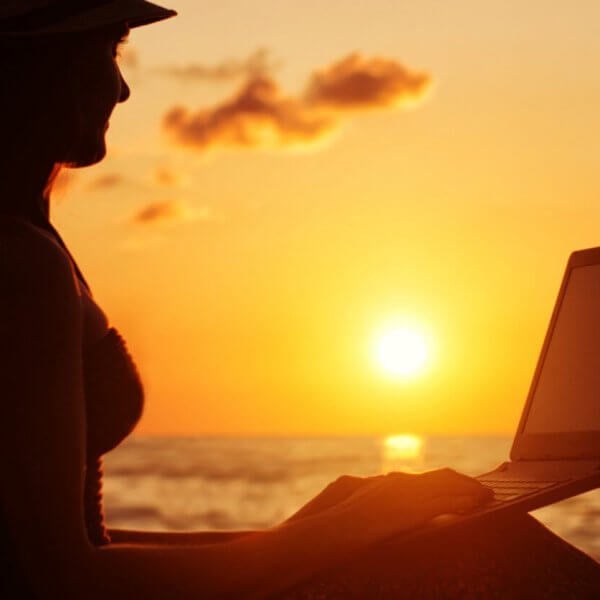 A woman is sitting on the beach with her laptop, enjoying the sunset in Siargao.