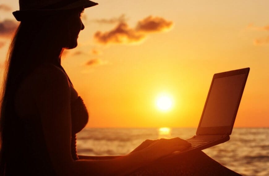 A woman is sitting on the beach with her laptop, enjoying the sunset in Siargao.