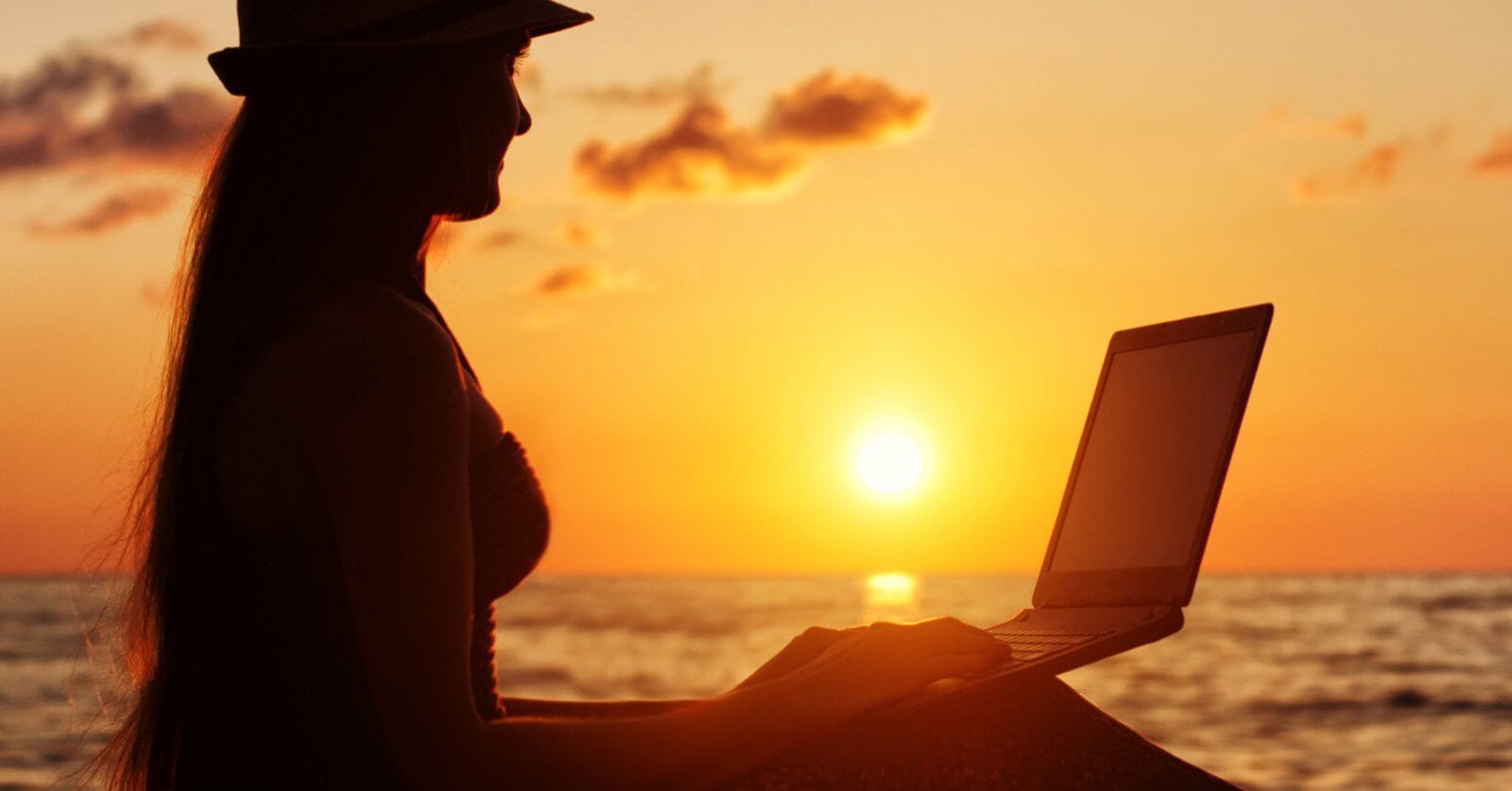 A woman is sitting on the beach with her laptop, enjoying the sunset in Siargao.