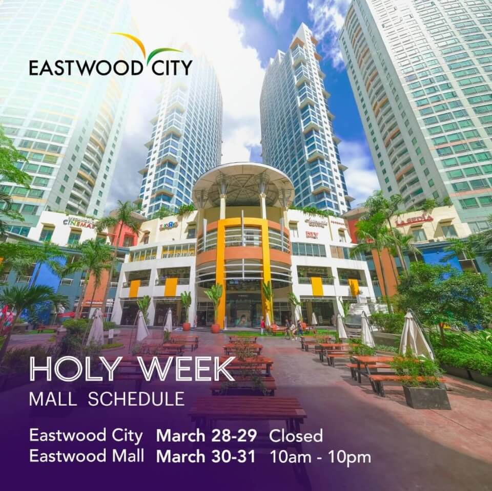 A vibrant urban public space with a mall announcement for holy week schedule, surrounded by towering skyscrapers under a clear blue sky.