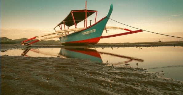 Beached traditional boat at low tide with reflection on water during Summer Break.