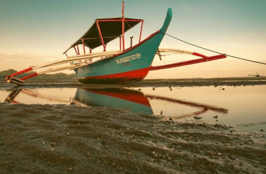Beached traditional boat at low tide with reflection on water during Summer Break.