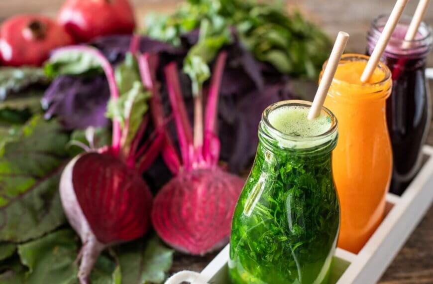 Three bottles of colorful vegetable juices—green, beetroot red, and orange—from top juice bars in Metro Manila, placed on a wooden table, surrounded by fresh vegetables like beets, carrots, and leafy greens.
