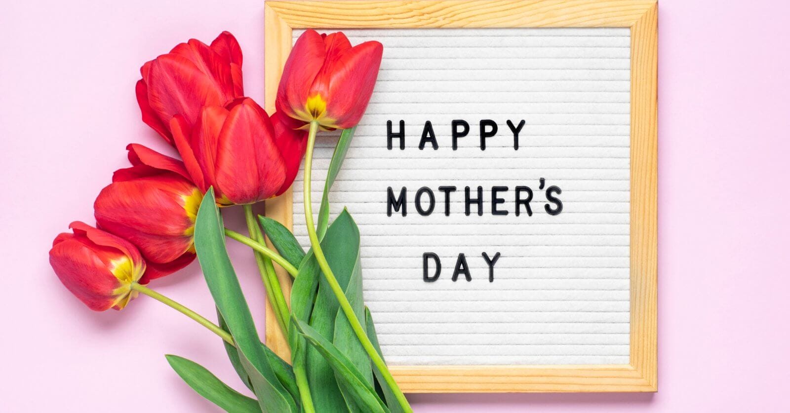 A Mother's Day celebration greeting with red tulips alongside a framed white letter board that reads "happy mother's day" on a pink background.