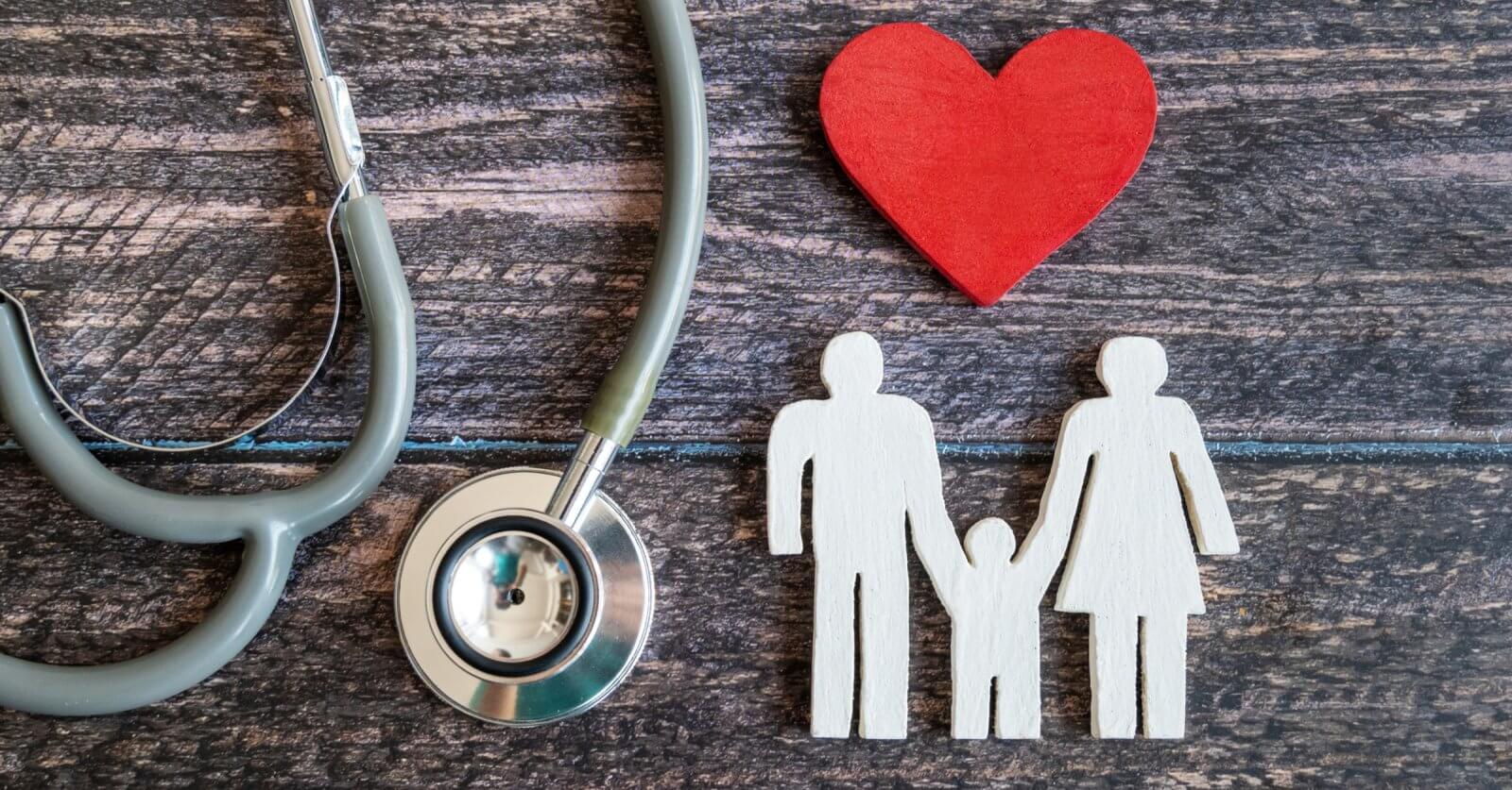 A stethoscope is positioned on the left side of the image, with its ear tubes and chest piece visible. A red wooden heart lies to the right of the stethoscope. Next to the heart, there's a white wooden cutout depicting a family of three holding hands. This scene evokes Hi-Precision Diagnostics centers in Metro Manila.