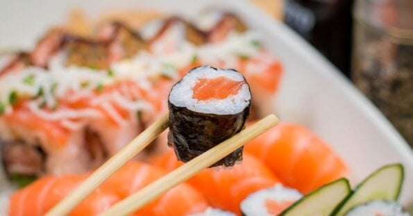 Close-up of chopsticks holding a sushi roll with a seaweed wrap, rice, and salmon filling. The background showcases various sushi pieces, including nigiri topped with raw salmon slices. This arrangement highlights the vibrant colors and freshness of Metro Manila's best Japanese restaurants.