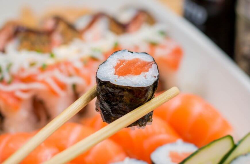 Close-up of chopsticks holding a sushi roll with a seaweed wrap, rice, and salmon filling. The background showcases various sushi pieces, including nigiri topped with raw salmon slices. This arrangement highlights the vibrant colors and freshness of Metro Manila's best Japanese restaurants.
