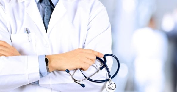 Close-up of an otolaryngologist wearing a white coat with a stethoscope draped around their neck. The doctor has their arms crossed, gripping the stethoscope. The background is blurred, featuring a bright, clinical setting in Metro Manila.