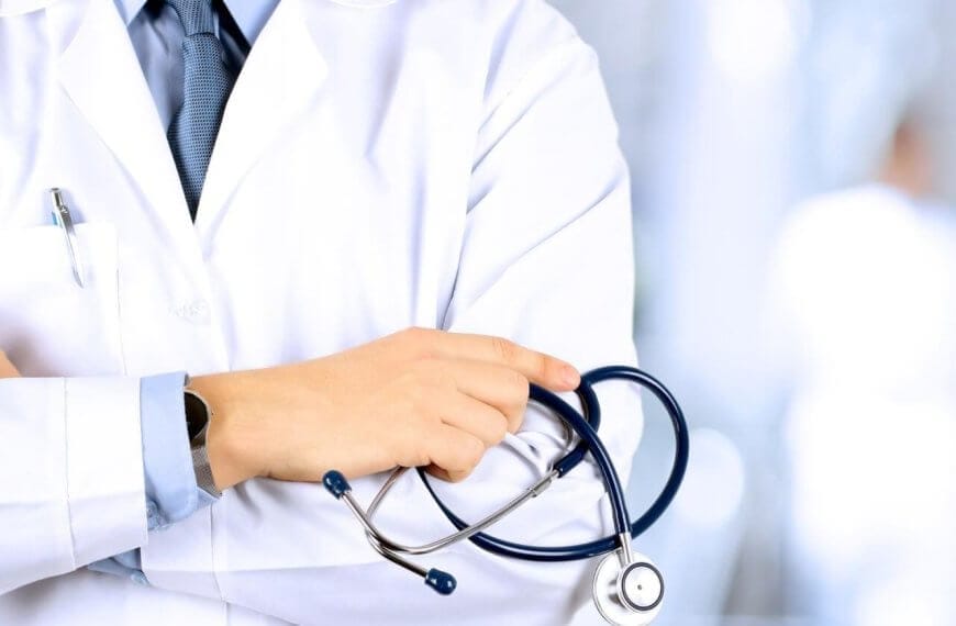 Close-up of an otolaryngologist wearing a white coat with a stethoscope draped around their neck. The doctor has their arms crossed, gripping the stethoscope. The background is blurred, featuring a bright, clinical setting in Metro Manila.
