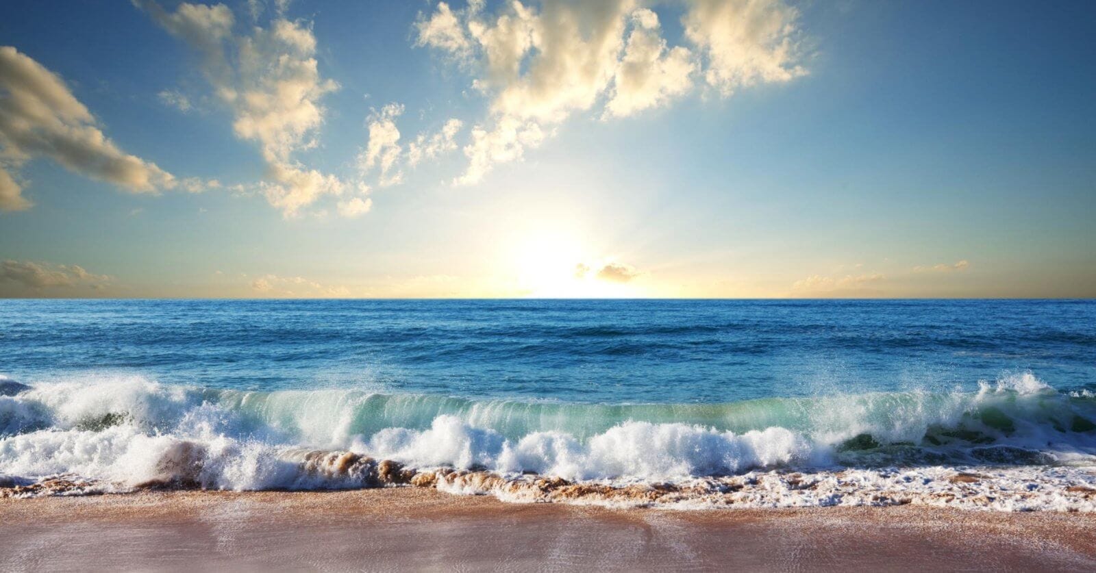 A scenic view of a Zambales beach at sunrise with gentle waves lapping the shore. The golden sunlight illuminates the sky, casting a warm glow on scattered clouds. The calm ocean stretches to the horizon, blending into the sky where the sun peeks just above the water's edge—truly one of the best Zambales resorts.