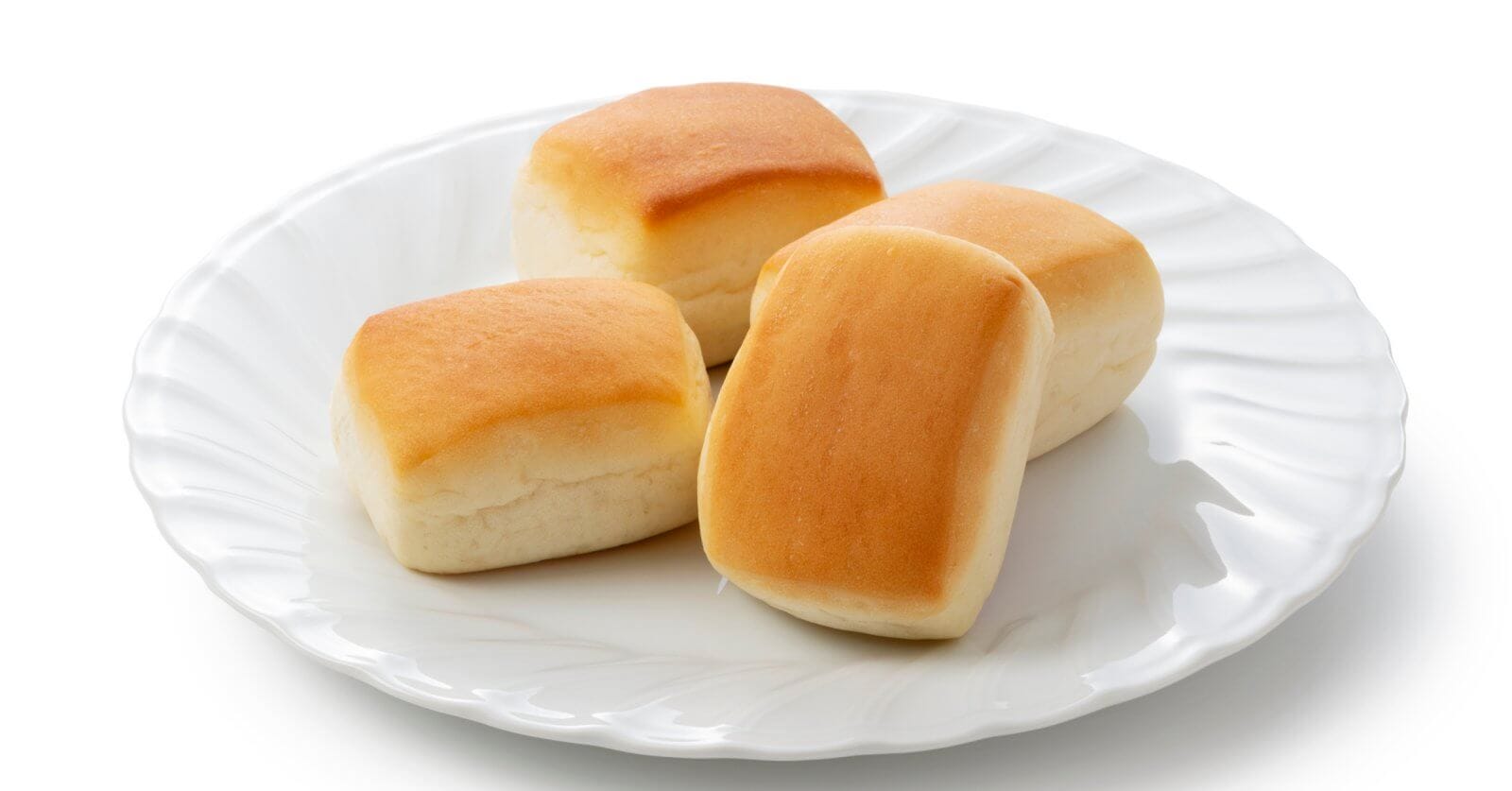 A white plate holds four golden-brown dinner rolls, each with a soft, fluffy texture. The rolls are slightly rectangular with rounded edges, and their tops are a light golden color that gradually lightens toward the bottom. Reminiscent of the best hot pandesal from Metro Manila's must-try bakeries, this plate features subtle decorative ridges around the rim.