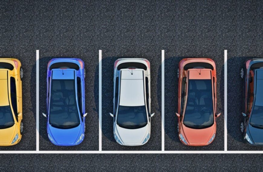 A top-down view of a parking lot shows five cars parked in a row, each in separate parking spots. The cars are, from left to right, yellow, blue, white, red, and black. The parking spots are outlined with white lines on the asphalt surface. It's a BGC designed for a stress-free experience.