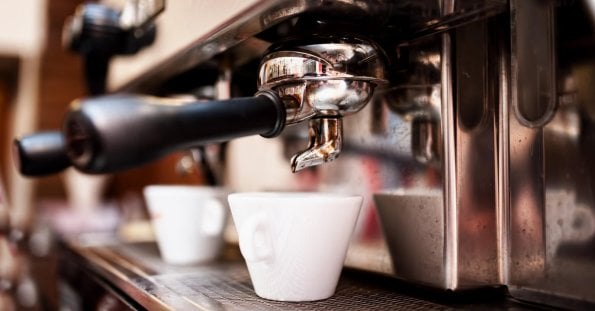 Close-up of a professional espresso machine in action, with a portafilter and spout dispensing coffee into a white ceramic cup below. The shiny metal surface of the machine reflects the bustling environment, hinting at Davao's best coffee place—a must-try for any café enthusiast.