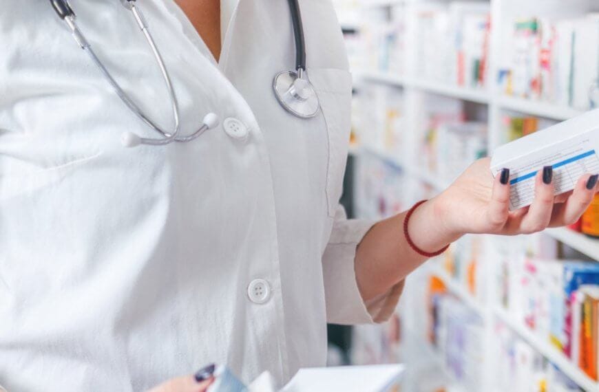 A pharmacist wearing a white coat and stethoscope is standing in a Mercury Branches pharmacy in Metro Manila. They are holding two boxes of medication while reading the label on one. Shelves filled with various medicine boxes are visible in the background.