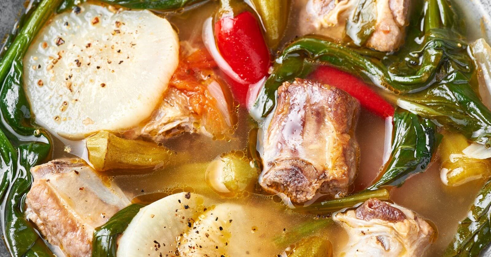 A bowl of steaming soup filled with chunks of pork ribs, radish slices, leafy greens, chili peppers, and celery stalks. The soup has a clear broth and is garnished with ground pepper. Perfectly well-cooked ingredients float in the savory liquid. Found at one of Paranaque's best restaurants near Parqal Mall.