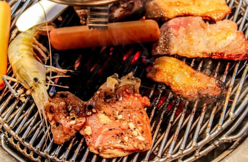 A grill loaded with various foods, including shrimp, sausage, and assorted cuts of Samgyupsal, all with visible seasoning. The grill grates have a shiny, metallic look as the food items cook to perfection, displaying grill marks and a slight char—a mouthwatering feast that could easily be found in Metro Manila.