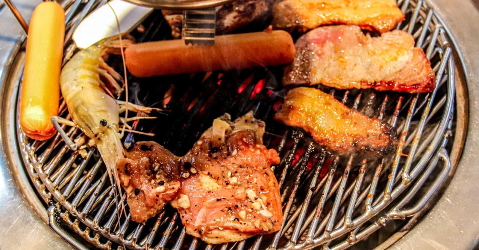 A grill loaded with various foods, including shrimp, sausage, and assorted cuts of Samgyupsal, all with visible seasoning. The grill grates have a shiny, metallic look as the food items cook to perfection, displaying grill marks and a slight char—a mouthwatering feast that could easily be found in Metro Manila.