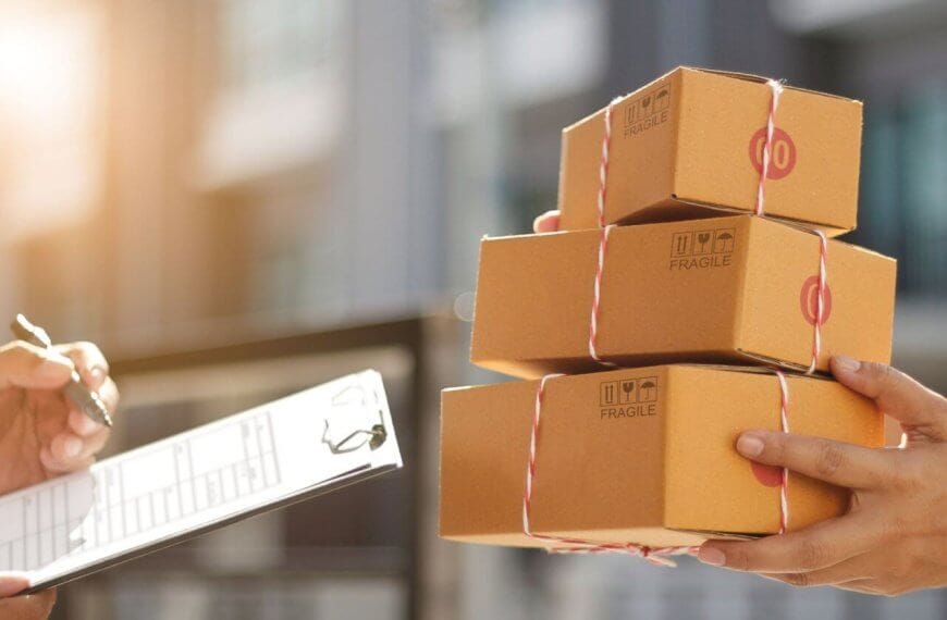 Close-up of two people at a Shopee Xpress drop-off point in Metro Manila, exchanging packages. One person holds three small cardboard boxes tied with red and white string, labeled "Fragile." The other person holds a clipboard and is using a pen, possibly signing or noting receipt of the packages. Sunlight is visible in the background.