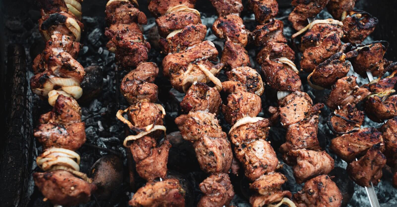 Several skewers of marinated meat and onions are being grilled over a bed of charcoal. The meat is slightly charred, giving it a deliciously cooked look with visible spices and seasoning. The skewers are spaced closely together, filling up the grill surface—just like you'd find at the best restaurants in Tomas Morato.
