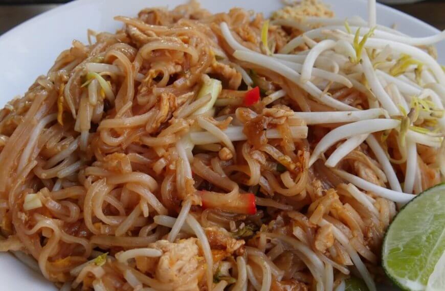 A plate of Pad Thai with rice noodles, bean sprouts, chicken pieces, and red pepper slices, garnished with a lime wedge on the side. The noodles are lightly coated in a brown sauce, and the bean sprouts are placed on top for a fresh crunch—enjoyed at one of the best Thai restaurants in Metro Manila.