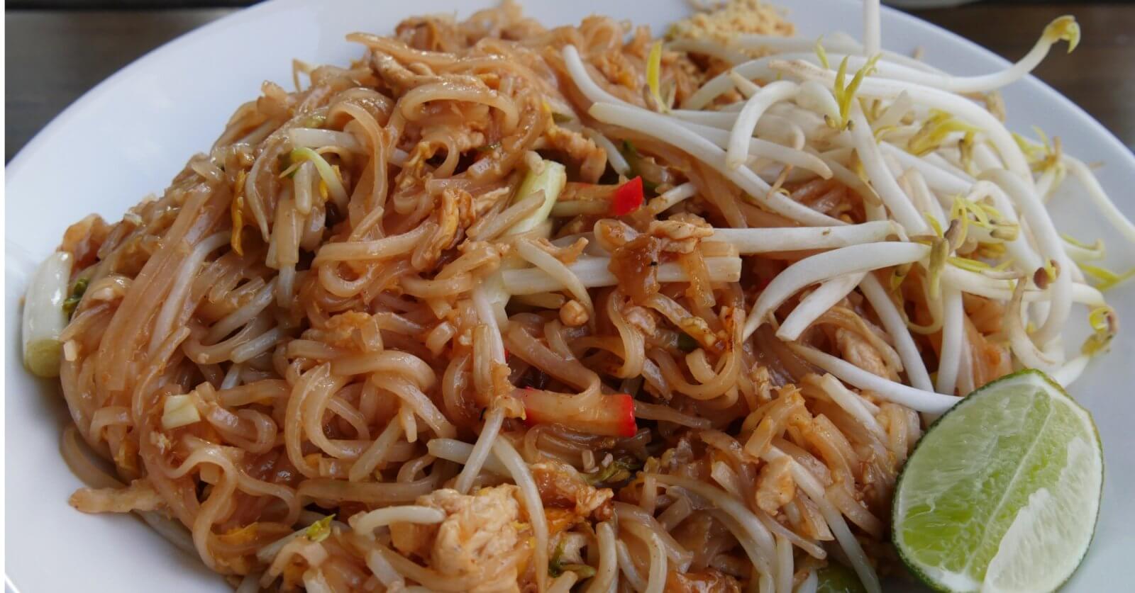 A plate of Pad Thai with rice noodles, bean sprouts, chicken pieces, and red pepper slices, garnished with a lime wedge on the side. The noodles are lightly coated in a brown sauce, and the bean sprouts are placed on top for a fresh crunch—enjoyed at one of the best Thai restaurants in Metro Manila.