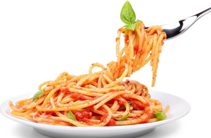 A fork twirls spaghetti topped with tomato sauce, garnished with a fresh basil leaf, lifted above a white plate filled with more spaghetti. The background is plain white, emphasizing the colorful dish—just like you'd experience at the best restaurants in One Ayala dining.