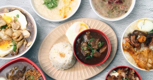 A variety of Filipino dishes, including rice, are displayed in bowls on a light gray surface. Central to this location is a plate with white rice, a hard-boiled egg, and a bowl of beef stew garnished with green onions. Surrounding dishes include different soups, stews, and meats with various toppings and garnishes.