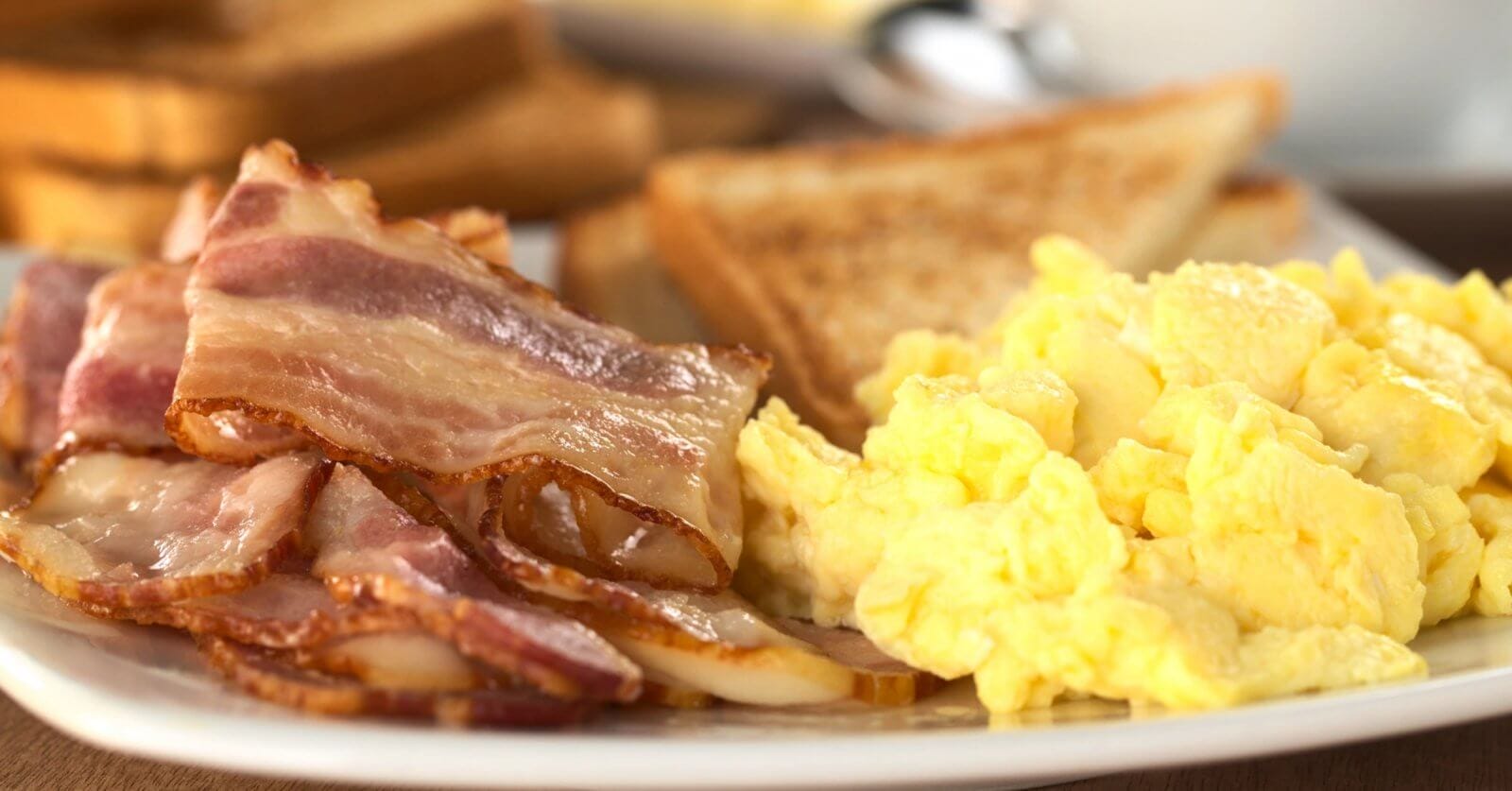 A breakfast plate from one of Marikina's top breakfast restaurants features fluffy scrambled eggs, several strips of crispy bacon with visible fatty edges, and golden brown toast with grill marks.