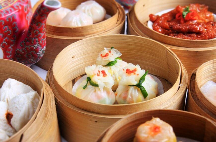 A variety of dimsum dishes are served in bamboo steamers. The dishes include dumplings, buns, and chicken feet. The dim sum items are intricately plated, with some garnished with a touch of red. A red, patterned teapot with Chinese characters is visible in the background—a typical scene in top 110 Chinese restaurants in Metro Manila.