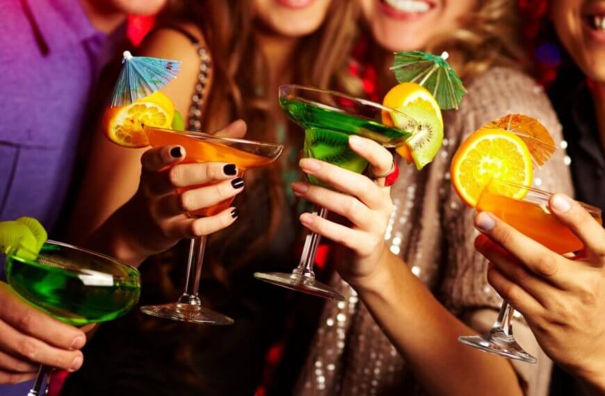 A group of people holding colorful cocktails, each garnished with citrus slices and tiny umbrellas, toast together. The scene is lively, with the group smiling and dressed in festive attire, suggesting a celebratory occasion or party. Located in Poblacion, this hotspot ranks among 115 must-visit bars for every occasion.