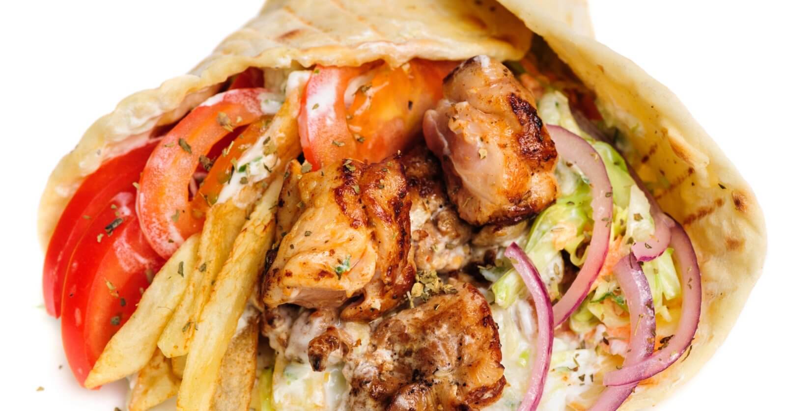 A close-up image of a gyro wrap featuring grilled pieces of seasoned meat, fresh tomato slices, red onion, lettuce, and a generous amount of fries. The ingredients are wrapped in a soft pita bread and drizzled with a creamy white sauce. This dish is one of the best places to enjoy shawarma in Metro Manila.