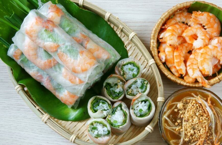 A woven tray holding fresh spring rolls filled with shrimp and vegetables rests atop a green banana leaf. Next to it, a small wicker bowl contains cooked shrimp, and another bowl is filled with brown peanut sauce garnished with crushed peanuts and sliced vegetables—a nod to authentic dining in Metro Manila's Vietnamese restaurants.